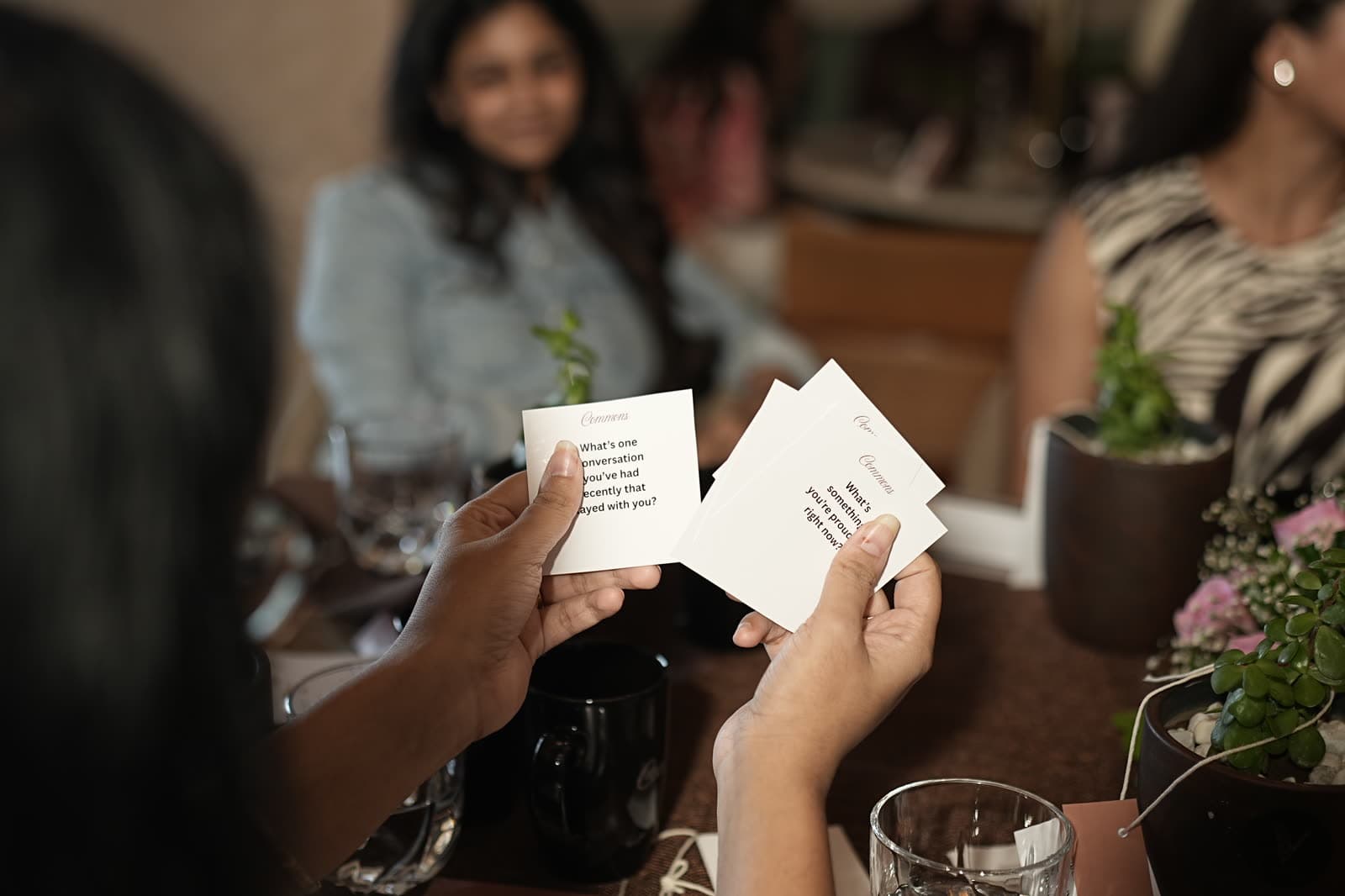 Hands holding conversation cards at the Commons Table.
