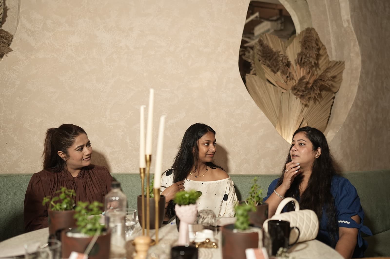 Three members talking across candles at the Commons Table.